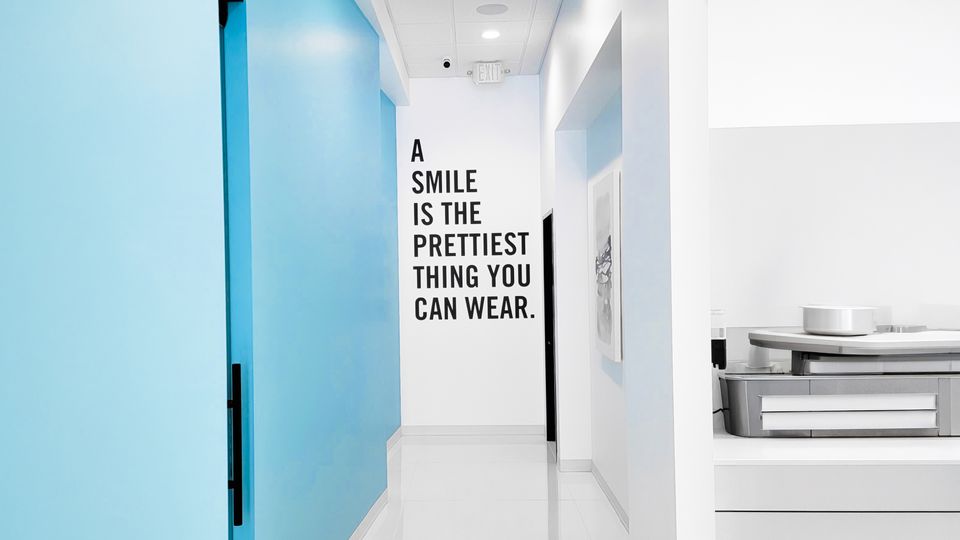 Bright dental office hallway with light blue accent wall and motivational quote reading "A Smile Is The Prettiest Thing You Can Wear"